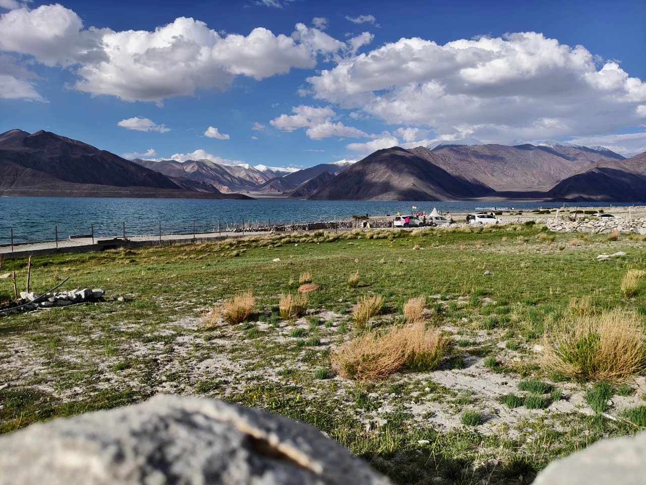 Blue water, open ground, and mountains near a lake in Ladakh.