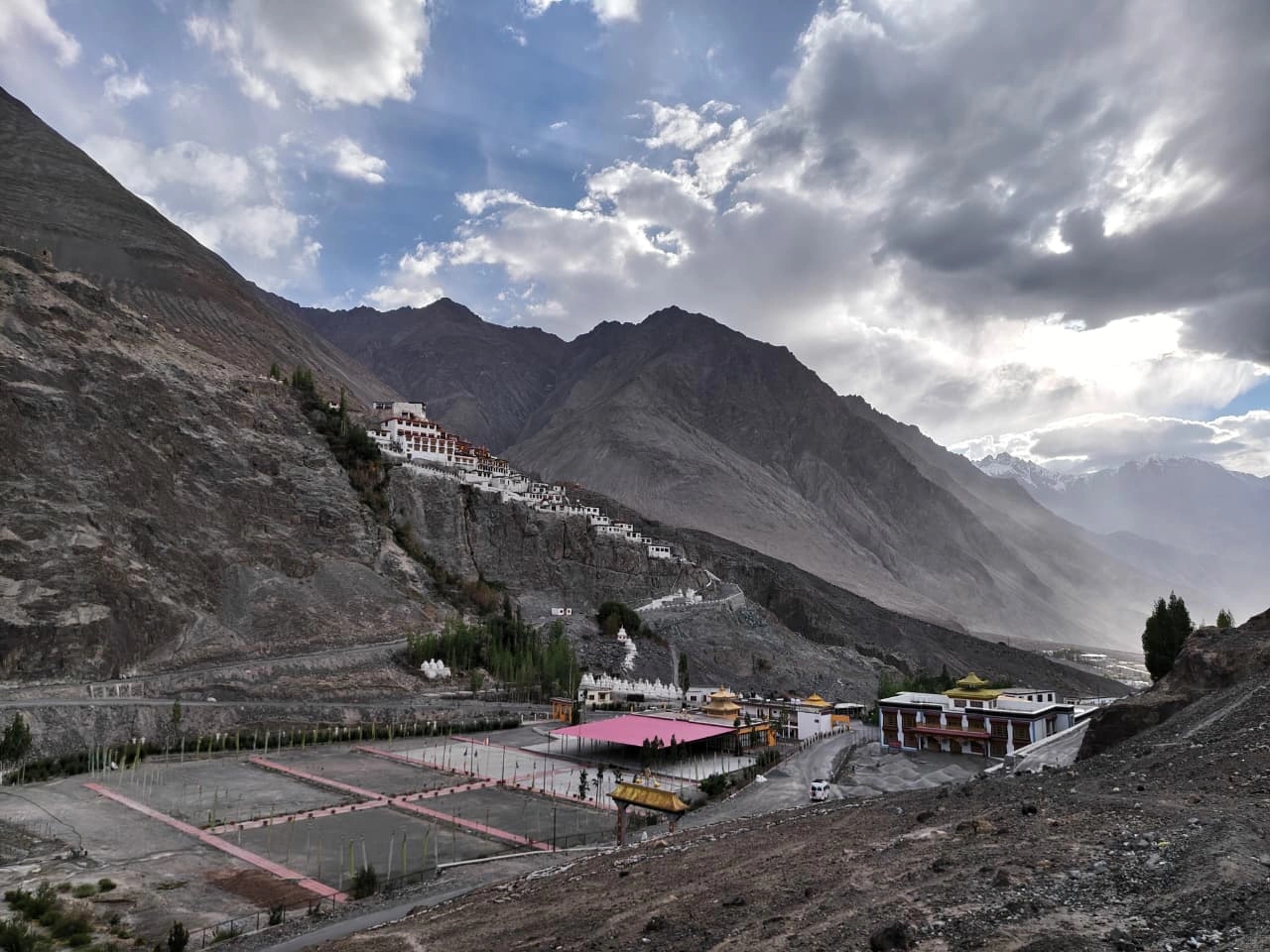 A monastery and settlement on a mountainside in Ladakh beneath a dramatic sky.